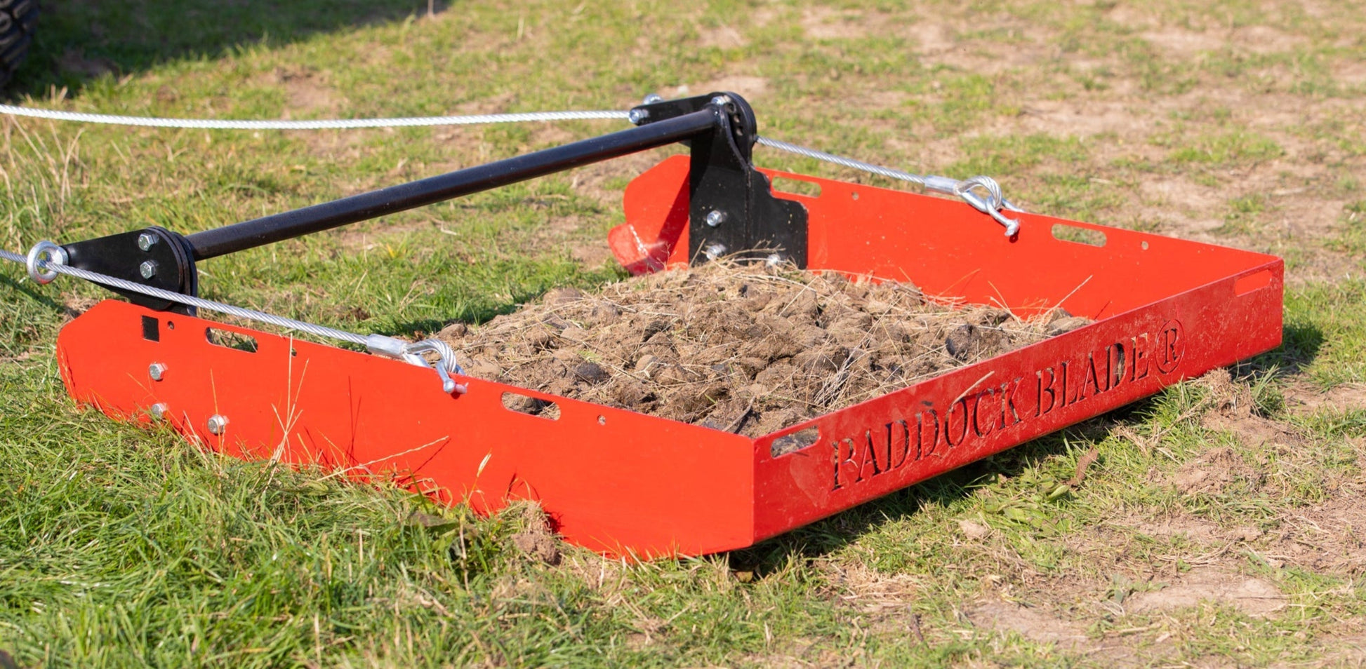 Paddock Blade in use on grassy field with scenic countryside backdrop